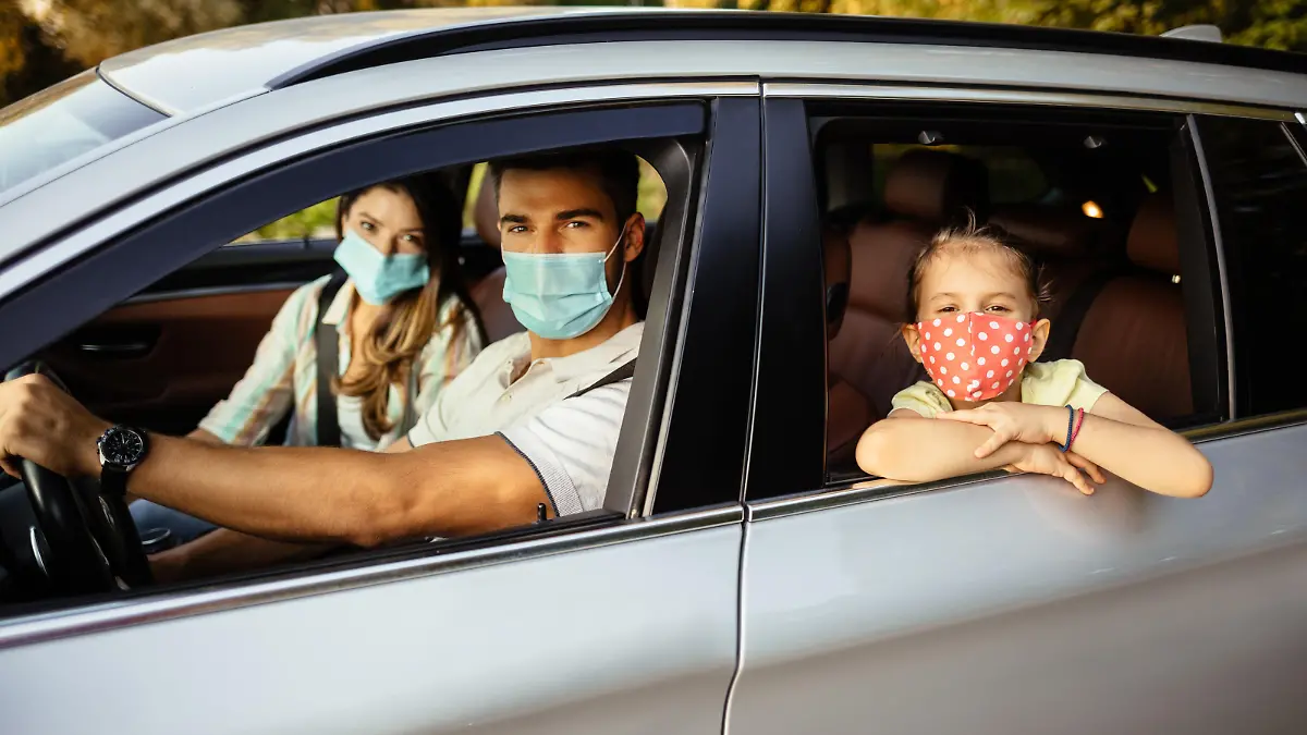 Familie sitzt mit Mundschutz in Auto