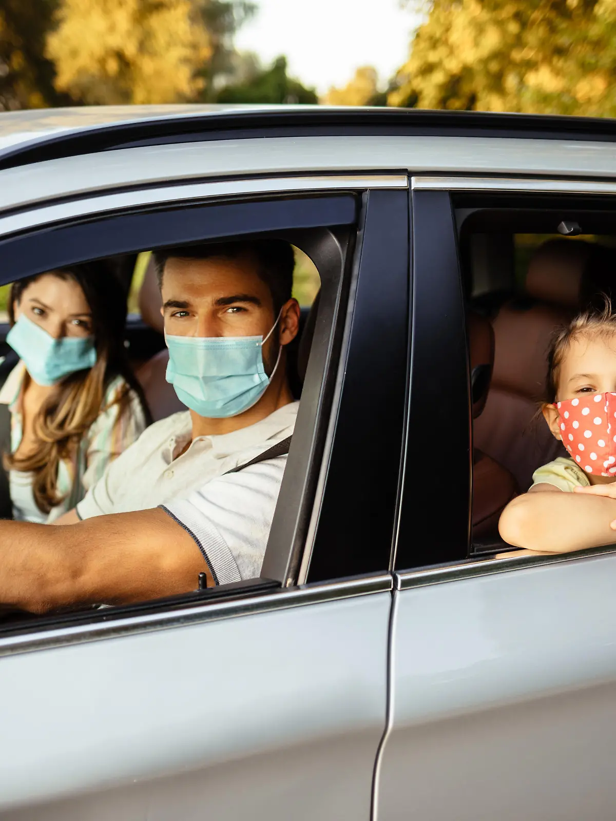 Familie sitzt mit Mundschutz in Auto