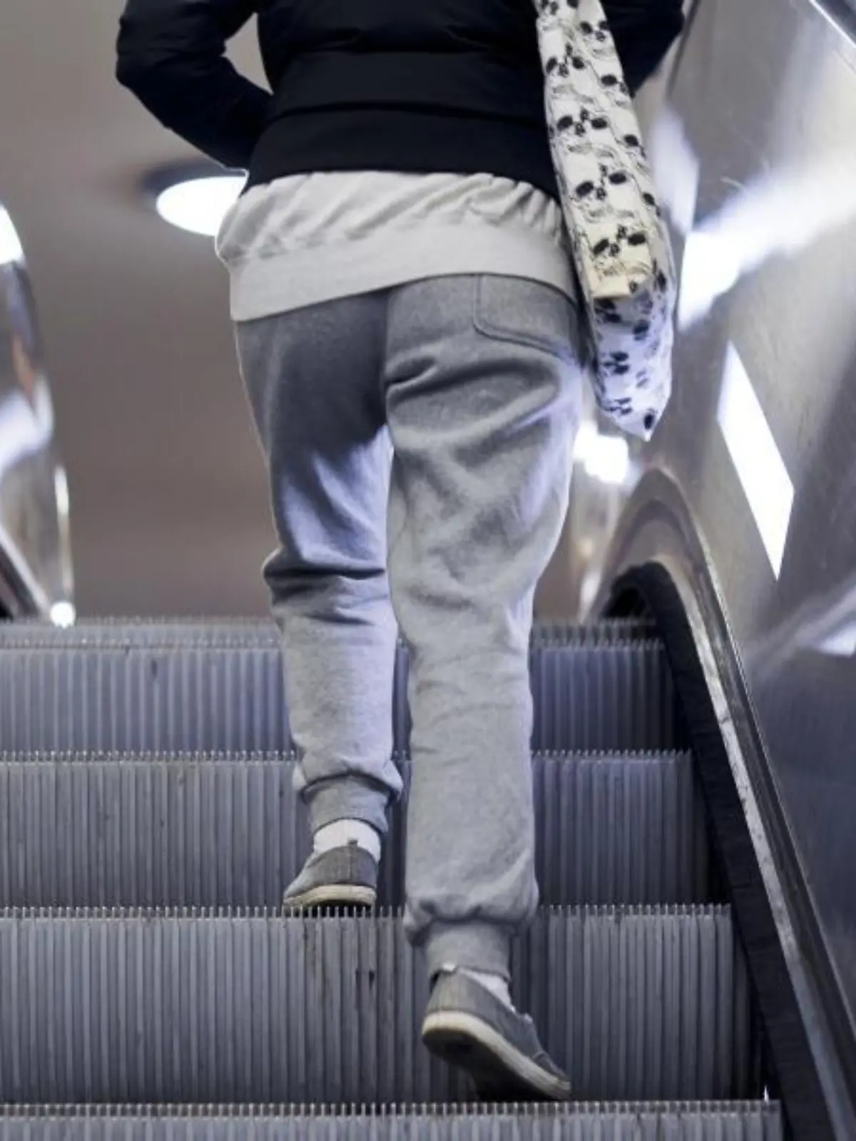 Eine Frau steht in Jogginghose auf einer Rolltreppe