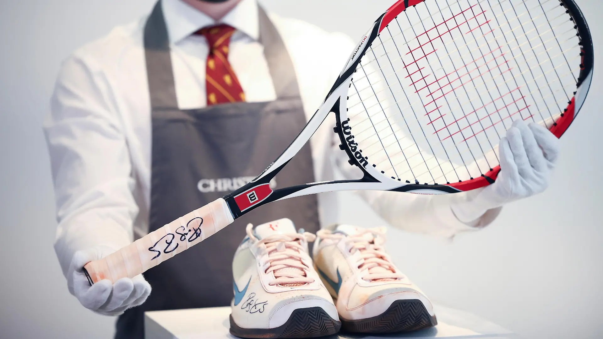 A Christie's gallery assistant poses with the racket and sneakers from the 'French Open, 2009' lot included in 'The Roger Federer Collection', due to be sold at auction, at Christie's auction house in London, Britain, April 27, 2021. Picture taken April 27, 2021. REUTERS/Henry Nicholls