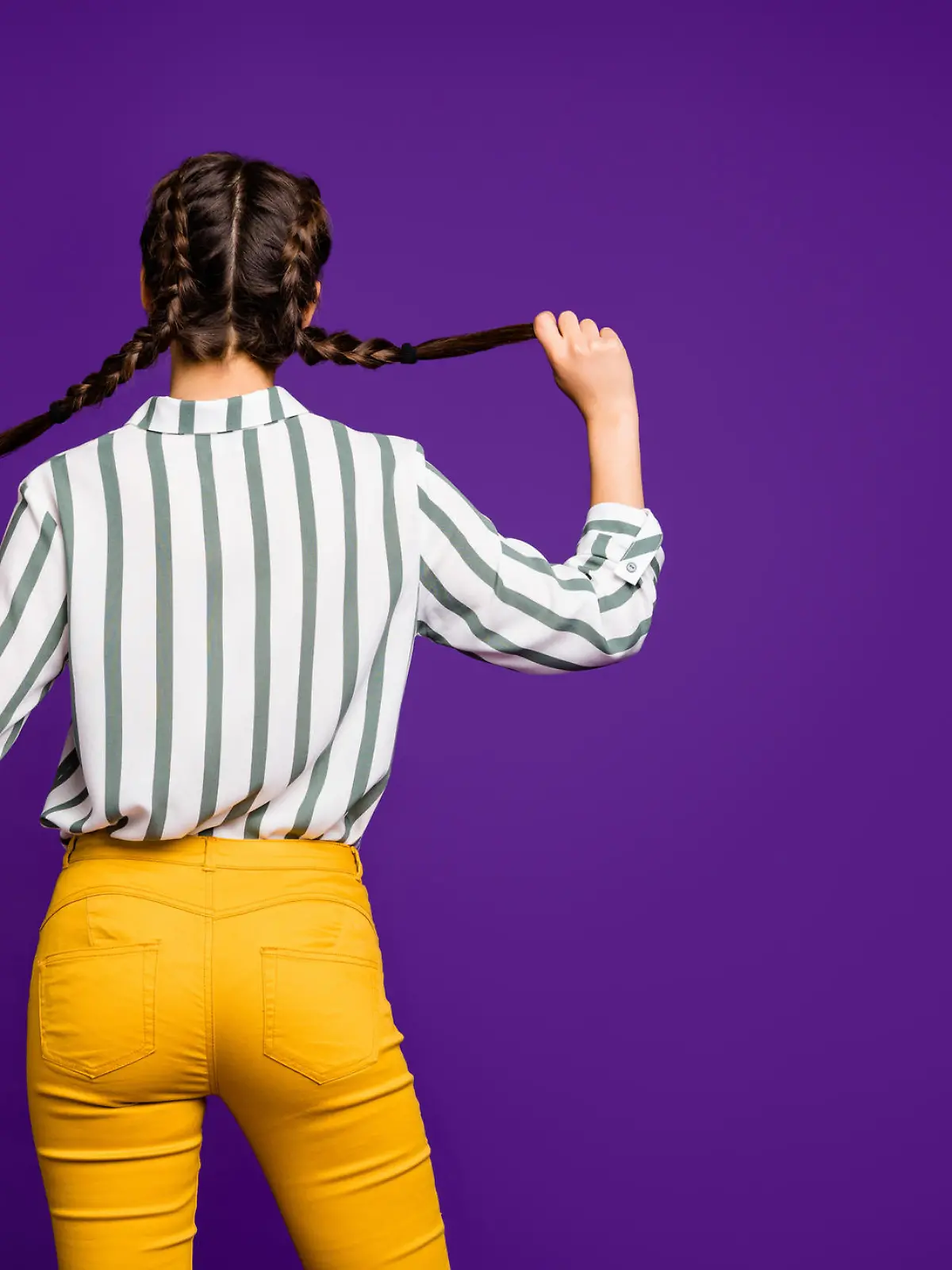 Rear behind view photo of beautiful pretty lady holding braids hands, hiding face shy person wear striped shirt yellow trousers isolated purple color background (Rear behind view photo of beautiful pretty lady holding braids hands, hiding face shy pe