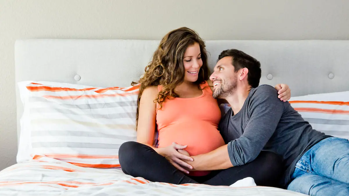Werdende Eltern sitzen auf dem Bett und streicheln  glücklich Babybauch der Mutter