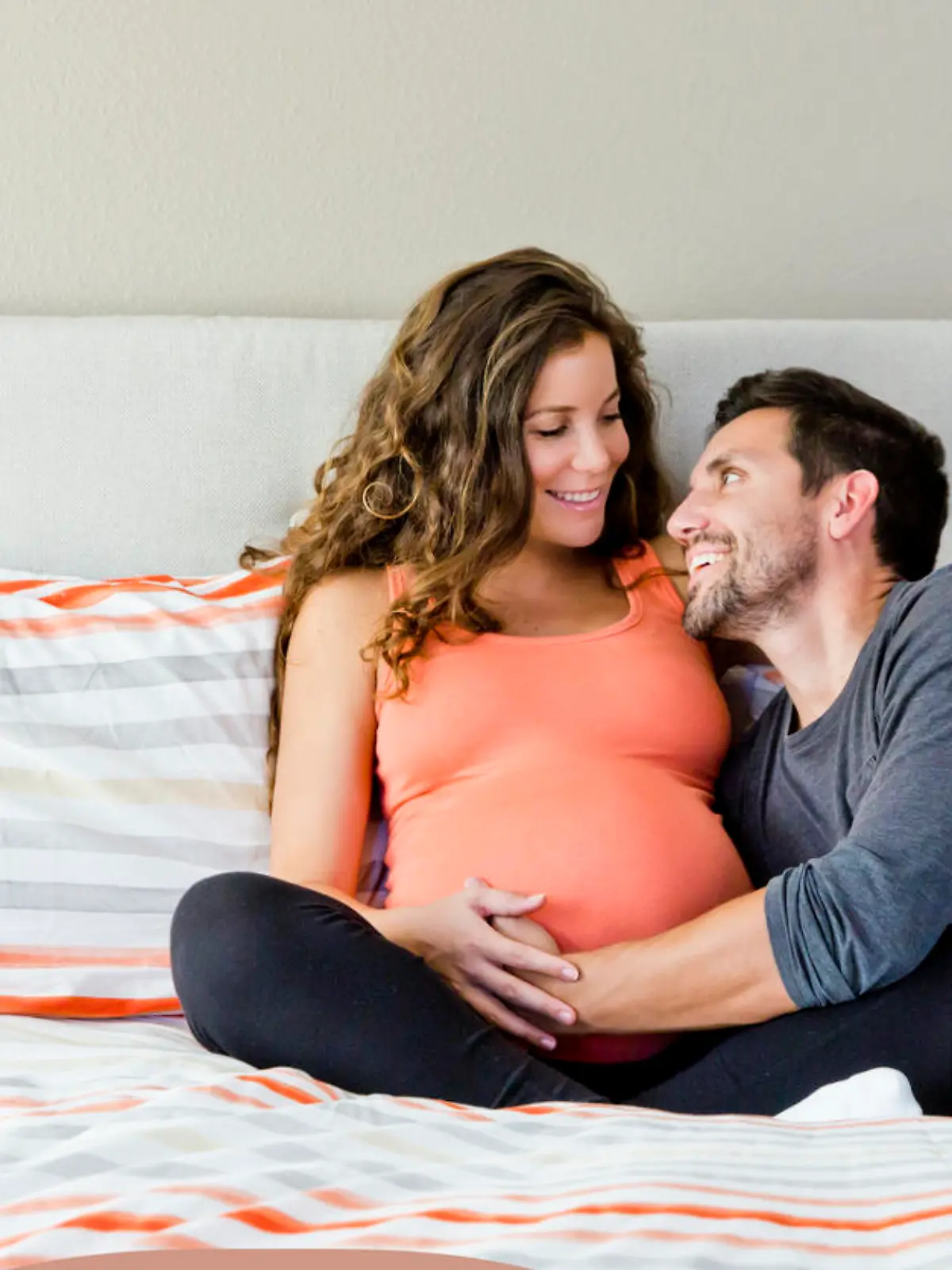 Werdende Eltern sitzen auf dem Bett und streicheln  glücklich Babybauch der Mutter