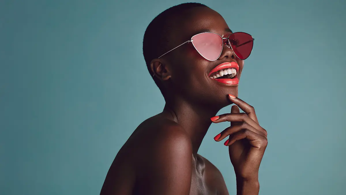 Schöne Frau mit Sonnenbrille vor blauem Hintergrund lacht.