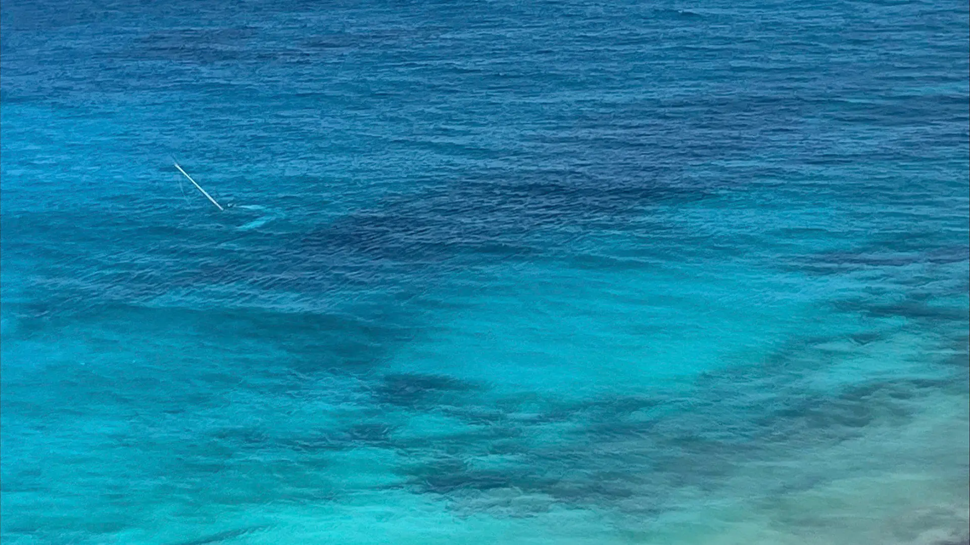 HANDOUT - 18.08.2023, Bahamas, Cay Sal: Dieses von der US-Küstenwache zur Verfügung gestellte Foto zeigt ein untergegangenes Segelboot während der Rettung eines 64-jährigen Mannes durch die Küstenwache. Die US-Küstenwache hat ein Foto mit einem «SOS»-Schriftzug veröffentlicht, der bei der Rettung eines gestrandeten Mannes von einer Bahamas-Insel geholfen hat. Der 64-Jährige habe drei Tage auf der Insel Cay Sal ausgeharrt und sei am Freitag gerettet worden, teilte die Küstenwache mit. Foto: Uncredited/U.S. Coast Guard/AP/dpa - ACHTUNG: Nur zur redaktionellen Verwendung und nur mit vollständiger Nennung des vorstehenden Credits +++ dpa-Bildfunk +++