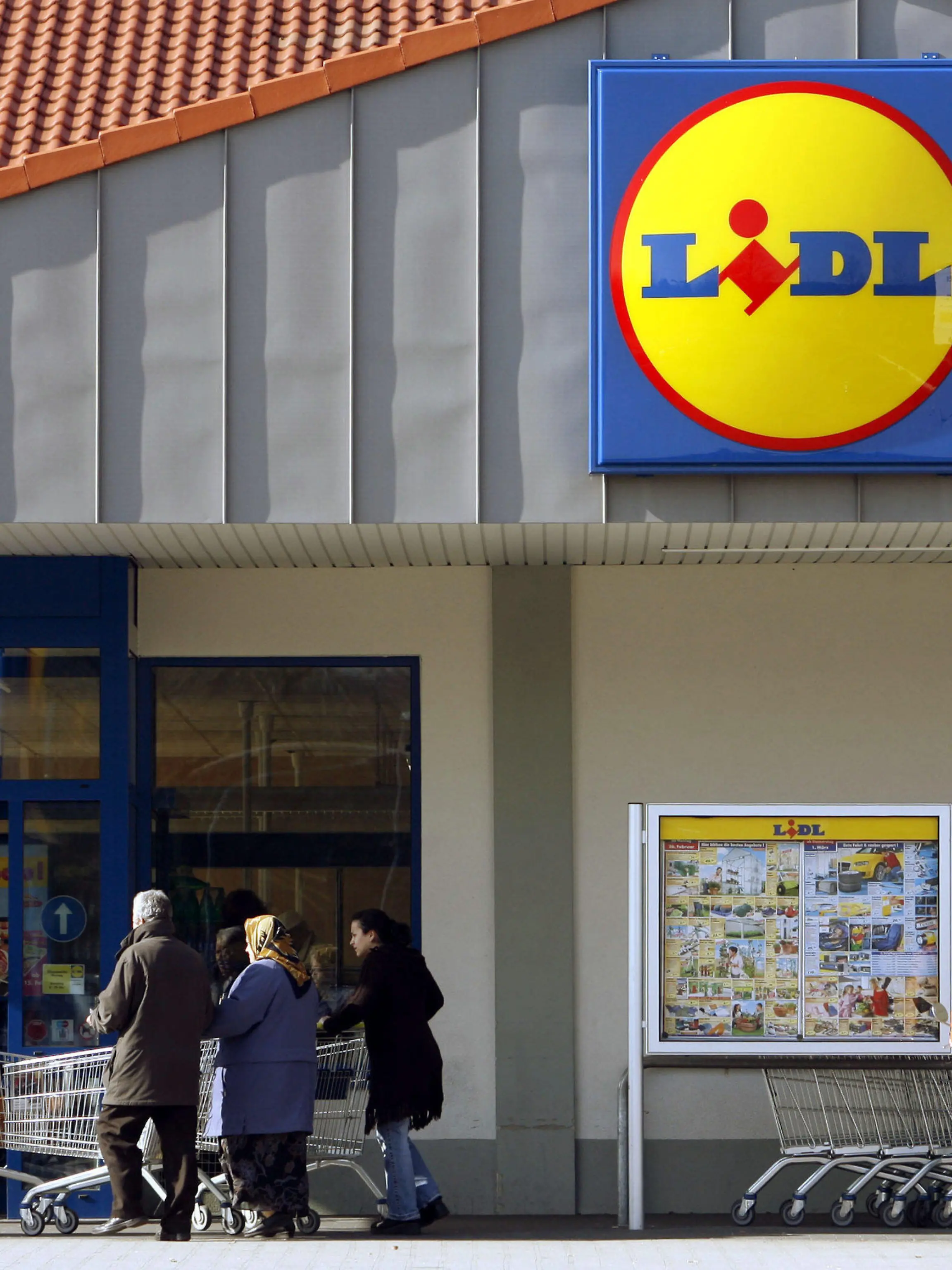 ARCHIV - ILLUSTRATION - Leute schieben am 22.02.2007 vor einem Lidl-Markt in Ludwigsburg ihre Einkaufswagen und ein Kunde schaut sich ein Werbeplakat an. Foto: Marijan Murat/ dpa   (zu dpa: "Discounter Lidl erpresst - Polizei nimmt Verdächtige fest") +++(c) dpa - Bildfunk+++