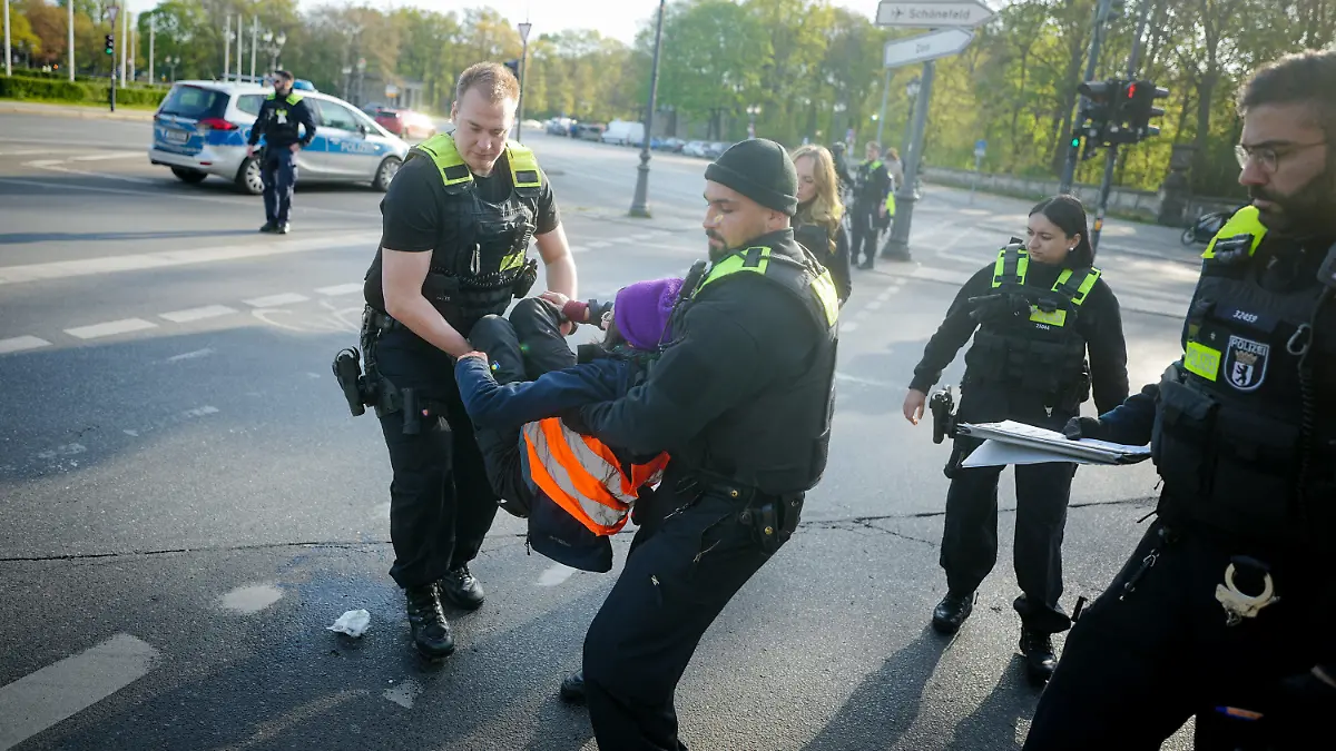 28.04.2023, Berlin: Polizeibeamte tragen eine Klimaaktivistin von der Straße am Großen Stern vor der Siegessäule. Hier haben sich zuvor Aktivisten der Klimabewegung Letzte Generation auf die Fahrbahn gesetzt und die Hand auf den Asphalt geklebt. Foto: Kay Nietfeld/dpa +++ dpa-Bildfunk +++