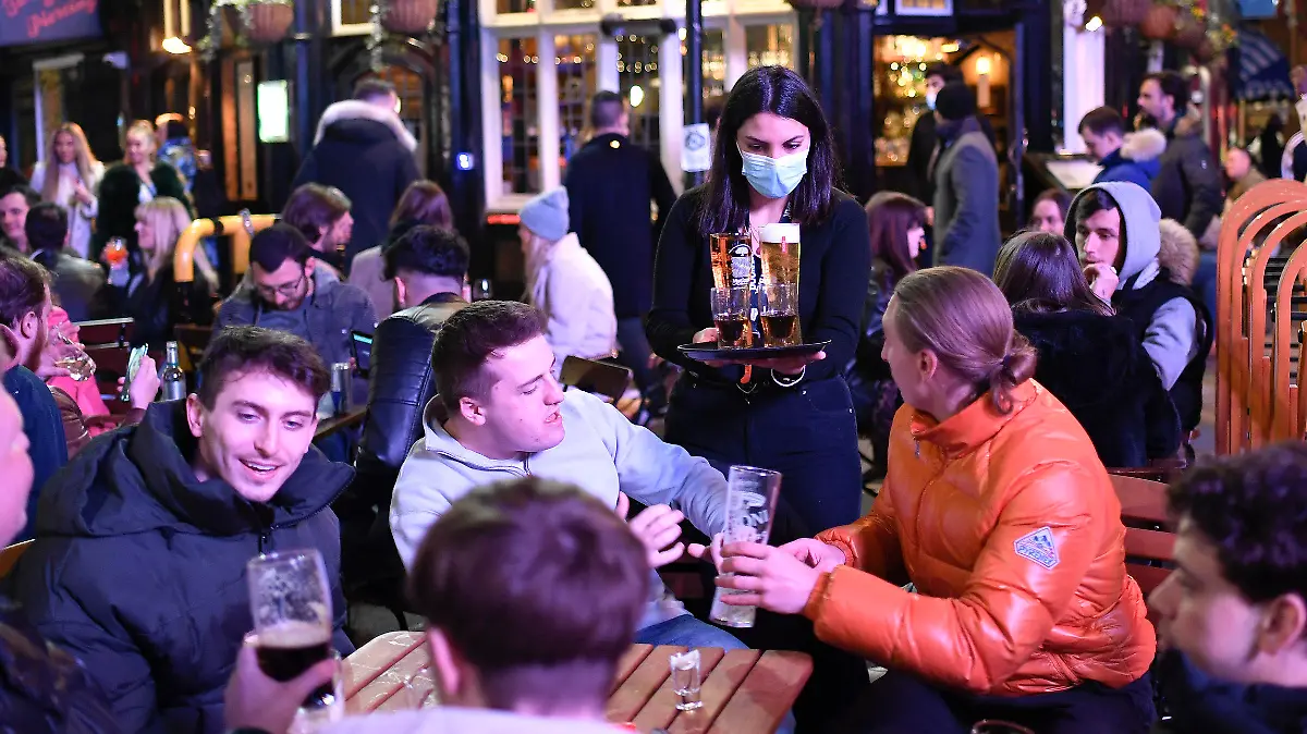 A waitress serves drinks as customers sit at setup tables outside pubs in Soho, in London, on the day some of England's third coronavirus lockdown restrictions were eased by the British government, Monday, April 12, 2021. People across England flocked to shed shaggy locks and browse for clothes, books and other "non-essential" items as shops, gyms, hairdressers, restaurant patios and beer gardens reopened Monday after months of lockdown. (AP Photo/Alberto Pezzali)