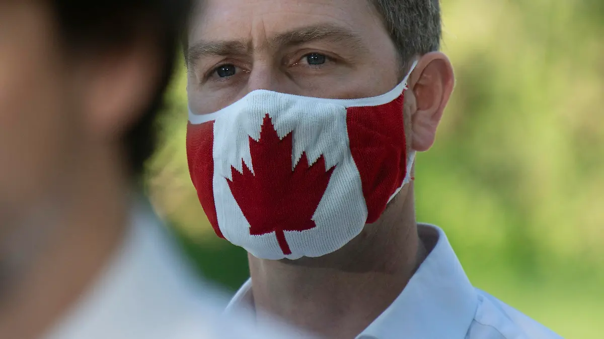 In this photo taken on June 19, 2020, Liberal Member of Parliament William Amos wears a Canadian flag mask as Prime Minister Justin Trudeau speaks during a news conference in Chelsea, Quebec. Amos, who has represented the Quebec district of Pontiac since 2015, appeared on the screens of his fellow lawmakers completely naked on Wednesday, April 14, 2021. He has apologized to his colleagues and says his video was accidentally turned on as he was changing into his work clothes after going for a jog. (Adrian Wyld/The Canadian Press via AP)