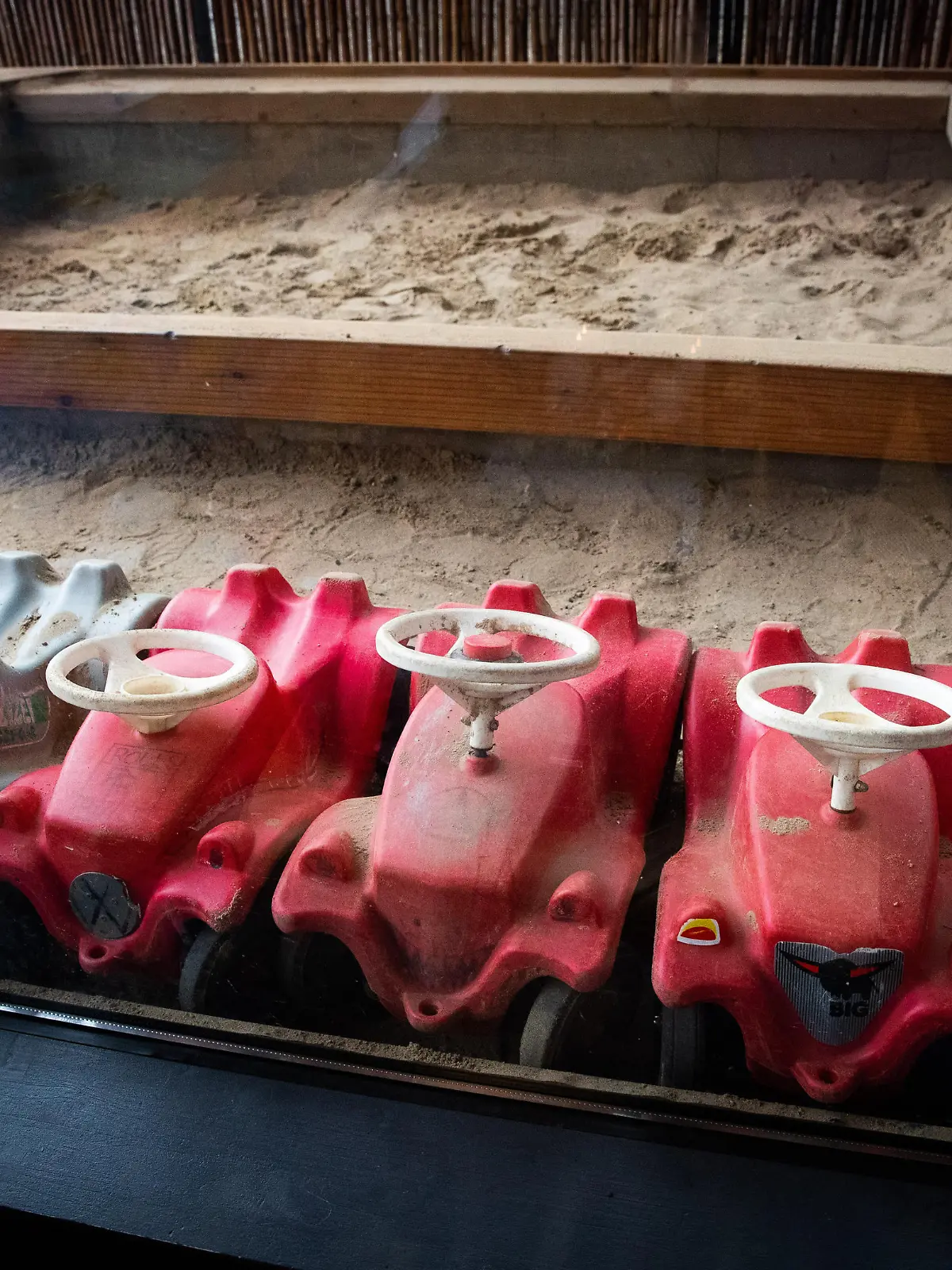 Mehrere Bobbycars stehen unter einem Vordach auf dem Spielplatz eines Kindergartens.