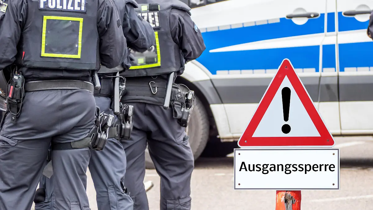 Polizei neben Warnschild, auf dem "Ausgangssperre" steht