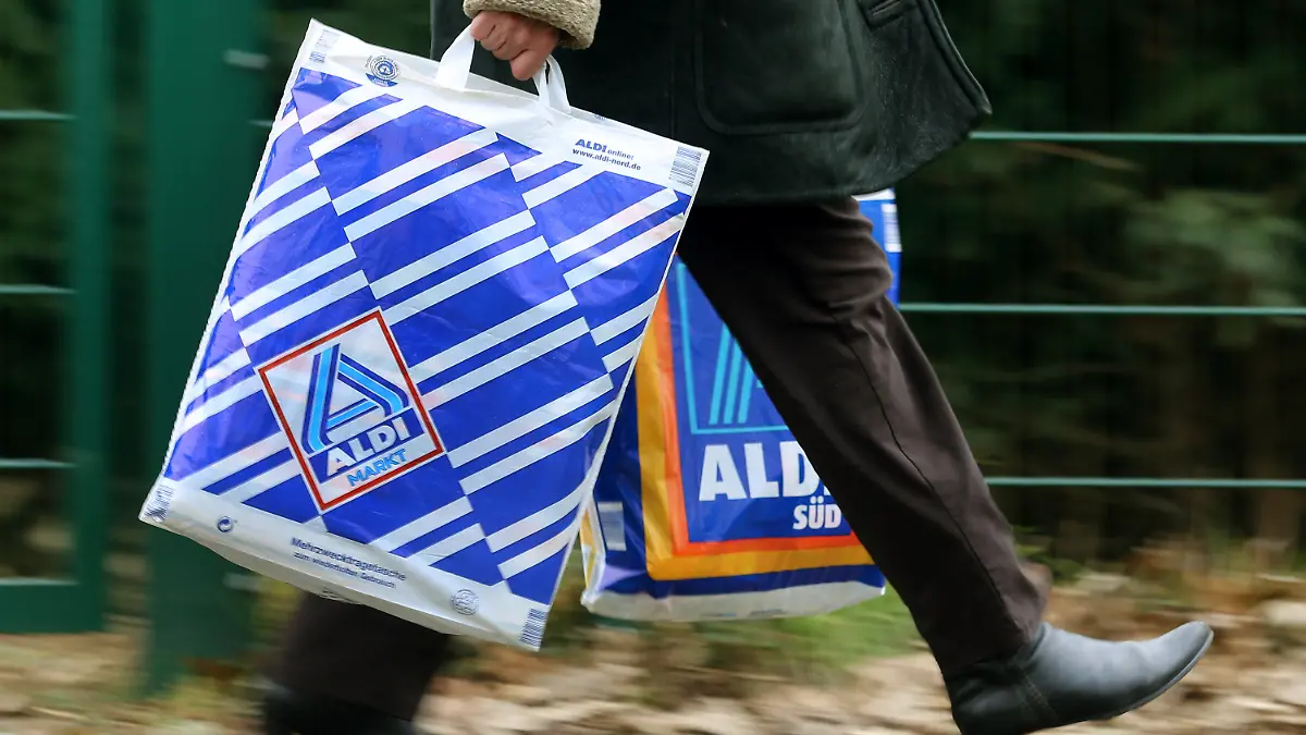 Die Kundin einer Aldi-Filiale trägt am 26.03.2013 in Essen (Nordrhein-Westfalen) in einer Einkaufstüte von Aldi-Nord und einer von Aldi-Süd ihre Einkäufe. Die Männer der Aldi-Erfolgsgeschichte sind die Söhne des Firmengründers Karl Albrecht: Seine Söhne Karl Junior und Theo. Foto: Roland Weihrauch/dpa (zu dpa-Korr:"Die Ursprünge von Aldi - 100 Jahre Familienunternehmen Albrecht.") +++(c) dpa - Bildfunk+++