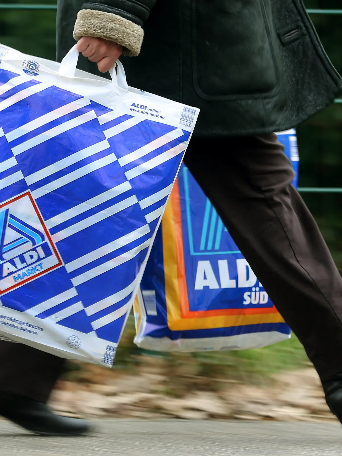 Die Kundin einer Aldi-Filiale trägt am 26.03.2013 in Essen (Nordrhein-Westfalen) in einer Einkaufstüte von Aldi-Nord und einer von Aldi-Süd ihre Einkäufe. Die Männer der Aldi-Erfolgsgeschichte sind die Söhne des Firmengründers Karl Albrecht: Seine Söhne Karl Junior und Theo. Foto: Roland Weihrauch/dpa (zu dpa-Korr:"Die Ursprünge von Aldi - 100 Jahre Familienunternehmen Albrecht.") +++(c) dpa - Bildfunk+++