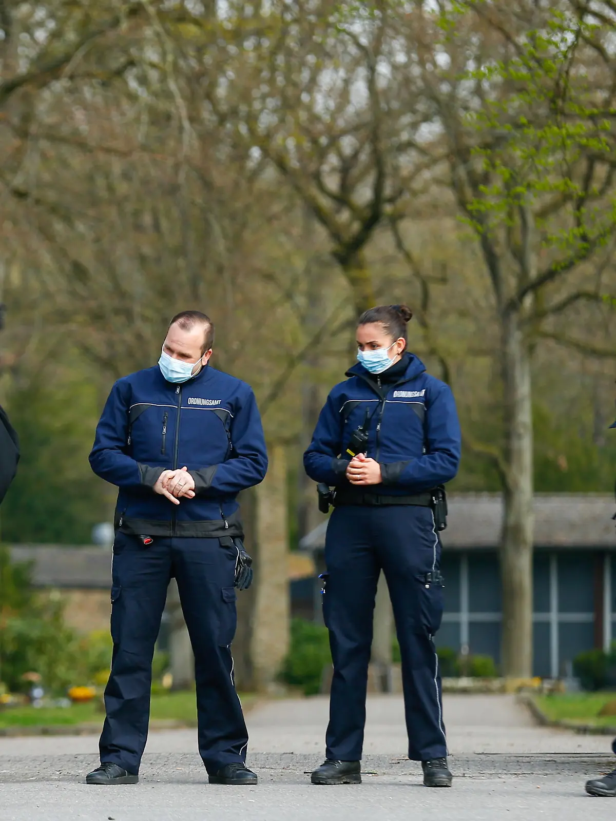 A priest enters a cemetery as public order staff secure the area while members and guests of the Goman clan wait to enter the funeral of one of the clan's chiefs, as only 25 people are allowed to attend due to coronavirus disease (COVID-19) restrictions, in Leverkusen, Germany, April 9, 2021. REUTERS/Thilo Schmuelgen