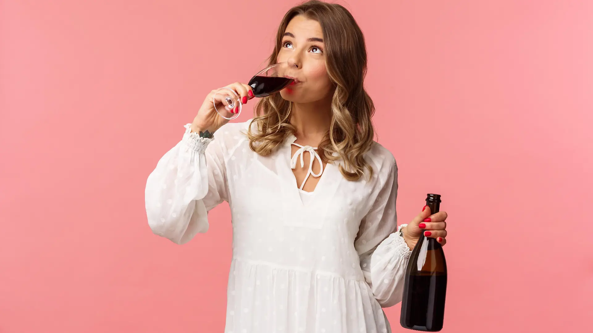 Holidays, spring and party concept. Portrait of young elegant happy blond woman, wear white trendy dress, drinking wine from glass looking up pleased, tasting good drink, hold bottle. (Holidays, spring and party concept. Portrait of young elegant hap