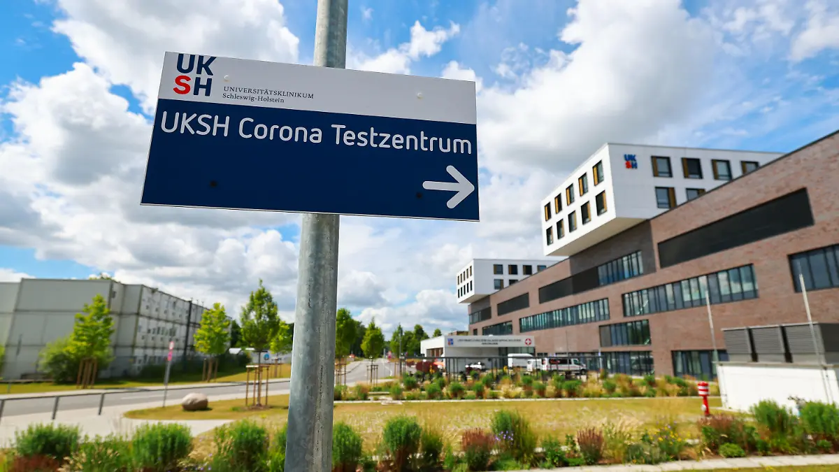 04.07.2022, Schleswig-Holstein, Lübeck: Ein Hinweisschild zum Corona Testzentrum steht neben dem Hauptgebäude mit Notaufnahme auf dem Gelände des Universitätsklinikum Schleswig-Holstein (UKSH) in Lübeck. Wegen Corona-Fällen in der Belegschaft ist die Lage in den Krankenhäusern in Schleswig-Holstein weiter angespannt. Foto: Christian Charisius/dpa +++ dpa-Bildfunk +++