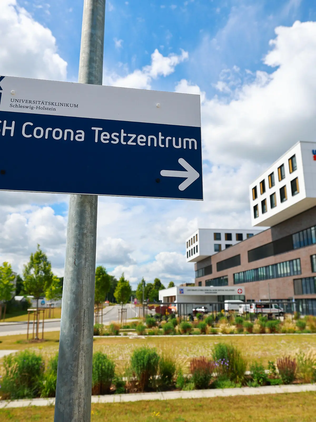 04.07.2022, Schleswig-Holstein, Lübeck: Ein Hinweisschild zum Corona Testzentrum steht neben dem Hauptgebäude mit Notaufnahme auf dem Gelände des Universitätsklinikum Schleswig-Holstein (UKSH) in Lübeck. Wegen Corona-Fällen in der Belegschaft ist die Lage in den Krankenhäusern in Schleswig-Holstein weiter angespannt. Foto: Christian Charisius/dpa +++ dpa-Bildfunk +++