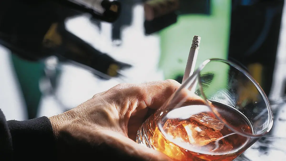 Eine Hand hält ein Glas mit Alkohol und eine Zigarette.