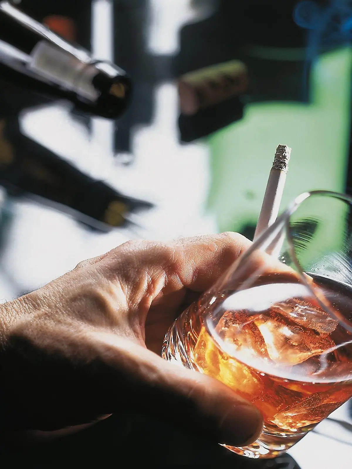 Eine Hand hält ein Glas mit Alkohol und eine Zigarette.