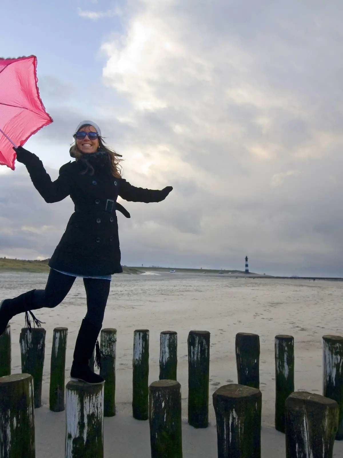 junge Frau mit rosa Schirm balanciert ueber Buhnen, Niederlande, Zeeland, Breskens | young woman with pink umbrella balancing on spur dikes, Netherlands, Zeeland, Breskens | Verwendung weltweit