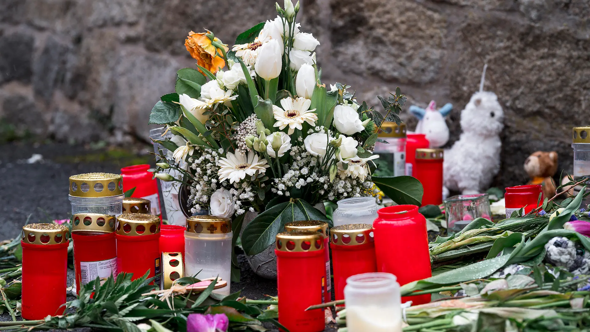 12.04.2023, Bayern, Wunsiedel: An der Straßenecke zur Zufahrtsstraße zum Kinder- und Jugendhilfezentrum, in dem eine Zehnjährige tot aufgefunden wurde, liegen Blumen, Kuscheltiere und Grablichter auf dem Gehweg. Foto: Daniel Vogl/dpa +++ dpa-Bildfunk +++