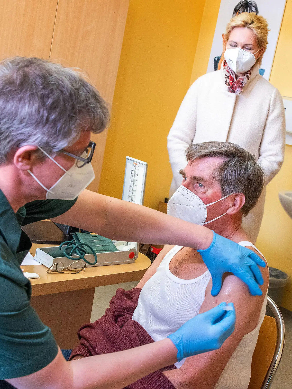 26.03.2021, Mecklenburg-Vorpommern, Neubukow: Manuela Schwesig (SPD), die Ministerpräsidentin von Mecklenburg-Vorpommern, beobachtet in der Hausarztpraxis von Stefan Zutz das Impfen des 79-jährigen Patienten Dietrich Peters mit dem Corona-Impfstoff AstraZeneca. Das landesweite Impfen bei den Hausärzten startet in Mecklenburg-Vorpommern, zunächst werden Starterpakete eingesetzt, mit denen sich das medizinische Personal schützen kann. Zusätzlich können damit in den Hausarztpraxen einige besonders gefährdete Patienten geimpft werden. Foto: Jens Büttner/dpa-Zentralbild/dpa +++ dpa-Bildfunk +++