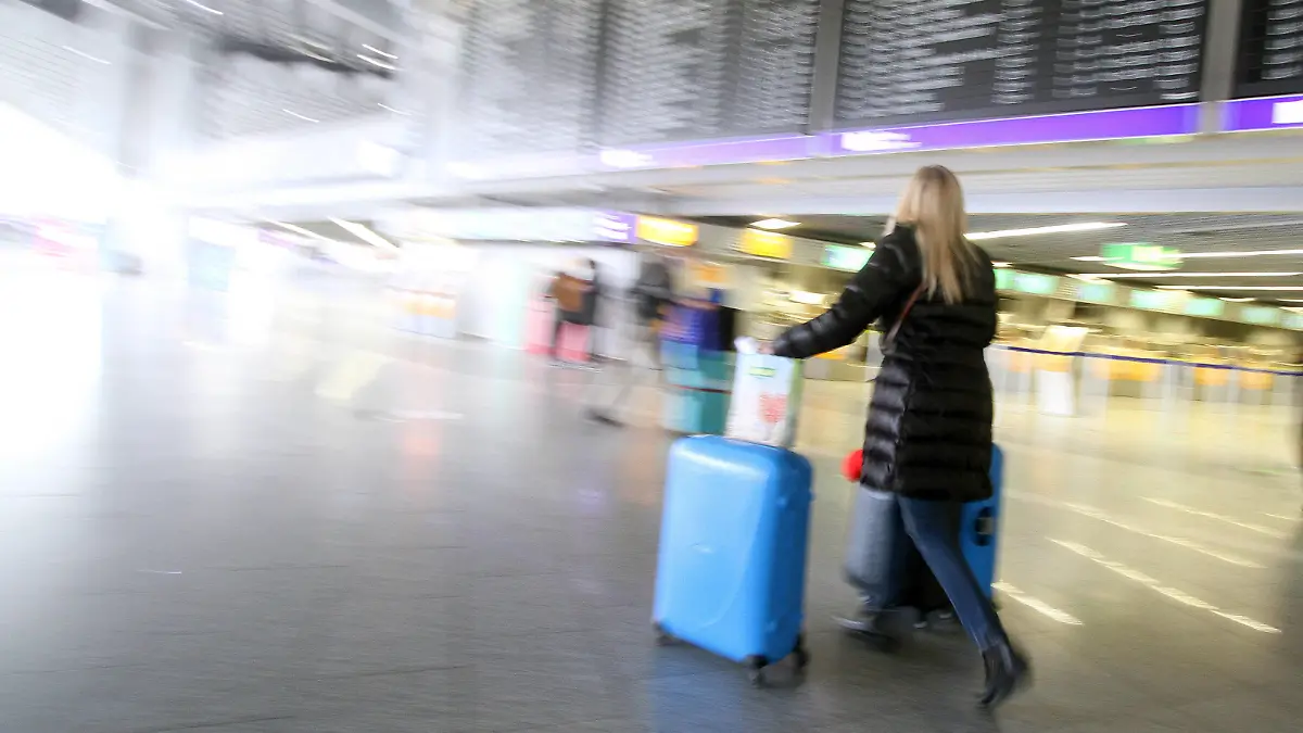 Eine Reisende geht mit ihrem Gepäck unter der Anzeigetafel in der Abflughalle B im Flughafen Frankfurt, Hessen, Deutschland *** A traveler walks with her luggage under the display board in Departure Hall B at Frankfurt Airport, Hesse, Germany
