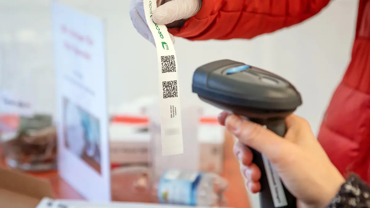 24.03.2021, Baden-Württemberg, Tübingen: Eine Frau scannt an einer Teststation den QR-Code eines Tagesticket-Armbands. Die Stadt stellt das Tagesticket auf ein digitales System um. Wer sich an einer der neun Stationen im Stadtgebiet auf Corona testen lässt, bekommt künftig ein Armband mit einem QR-Code, welches nicht weitergegeben werden kann. Foto: Christoph Schmidt/dpa - ACHTUNG: Nummer unter QR-Code wurde aus rechtlichen Gründen gepixelt +++ dpa-Bildfunk +++