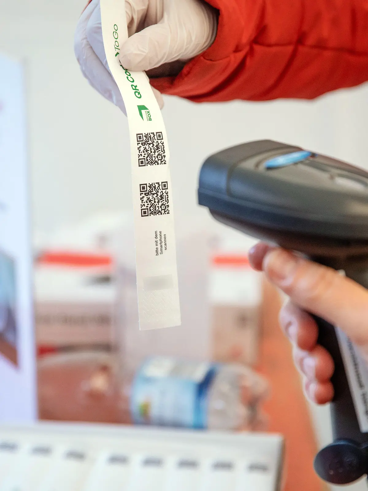 24.03.2021, Baden-Württemberg, Tübingen: Eine Frau scannt an einer Teststation den QR-Code eines Tagesticket-Armbands. Die Stadt stellt das Tagesticket auf ein digitales System um. Wer sich an einer der neun Stationen im Stadtgebiet auf Corona testen lässt, bekommt künftig ein Armband mit einem QR-Code, welches nicht weitergegeben werden kann. Foto: Christoph Schmidt/dpa - ACHTUNG: Nummer unter QR-Code wurde aus rechtlichen Gründen gepixelt +++ dpa-Bildfunk +++