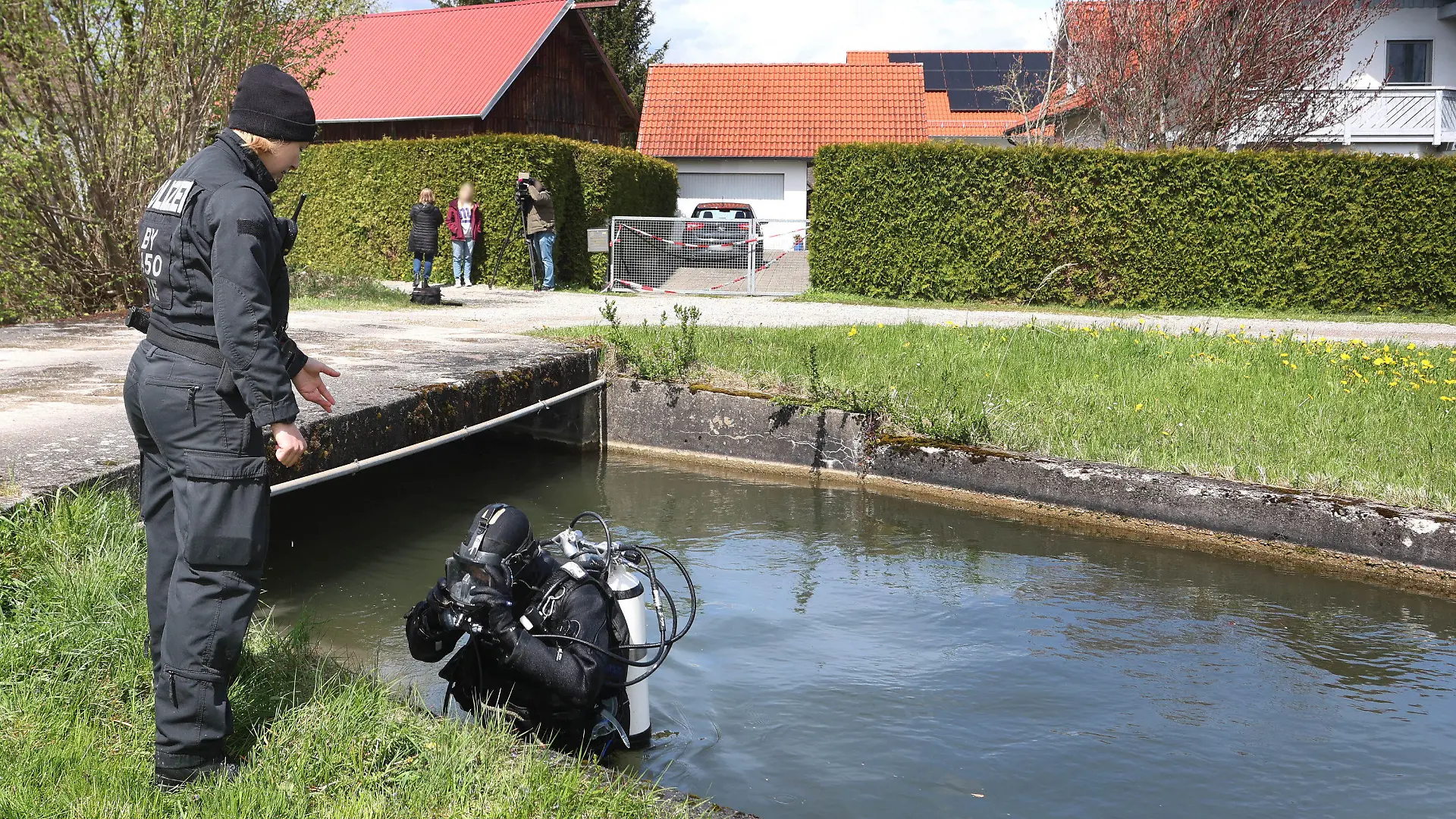 24.04.2023, Bayern, Altenstadt An Der Iller: Ein Polizeitaucher steigt vor einem Einfamilienhaus aus dem Wasser des Mühlbachs. Am Samstag wurden die Leichen eines Ehepaars in dem Haus entdeckt. Die Polizei geht davon aus, dass die beiden getötet wurden. Foto: Karl-Josef Hildenbrand/dpa - ACHTUNG: Person(en) wurde(n) aus rechtlichen Gründen gepixelt +++ dpa-Bildfunk +++