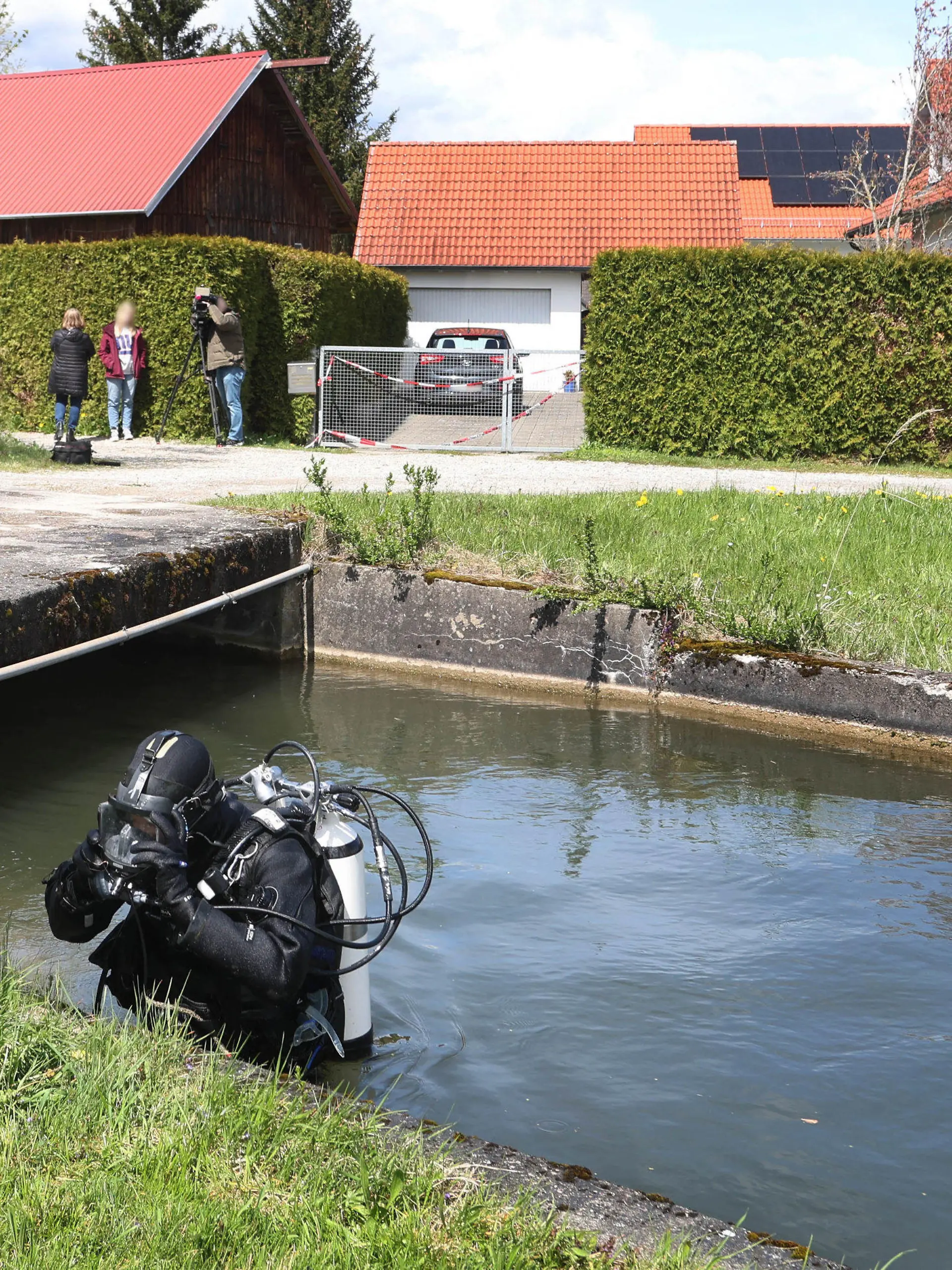 24.04.2023, Bayern, Altenstadt An Der Iller: Ein Polizeitaucher steigt vor einem Einfamilienhaus aus dem Wasser des Mühlbachs. Am Samstag wurden die Leichen eines Ehepaars in dem Haus entdeckt. Die Polizei geht davon aus, dass die beiden getötet wurden. Foto: Karl-Josef Hildenbrand/dpa - ACHTUNG: Person(en) wurde(n) aus rechtlichen Gründen gepixelt +++ dpa-Bildfunk +++