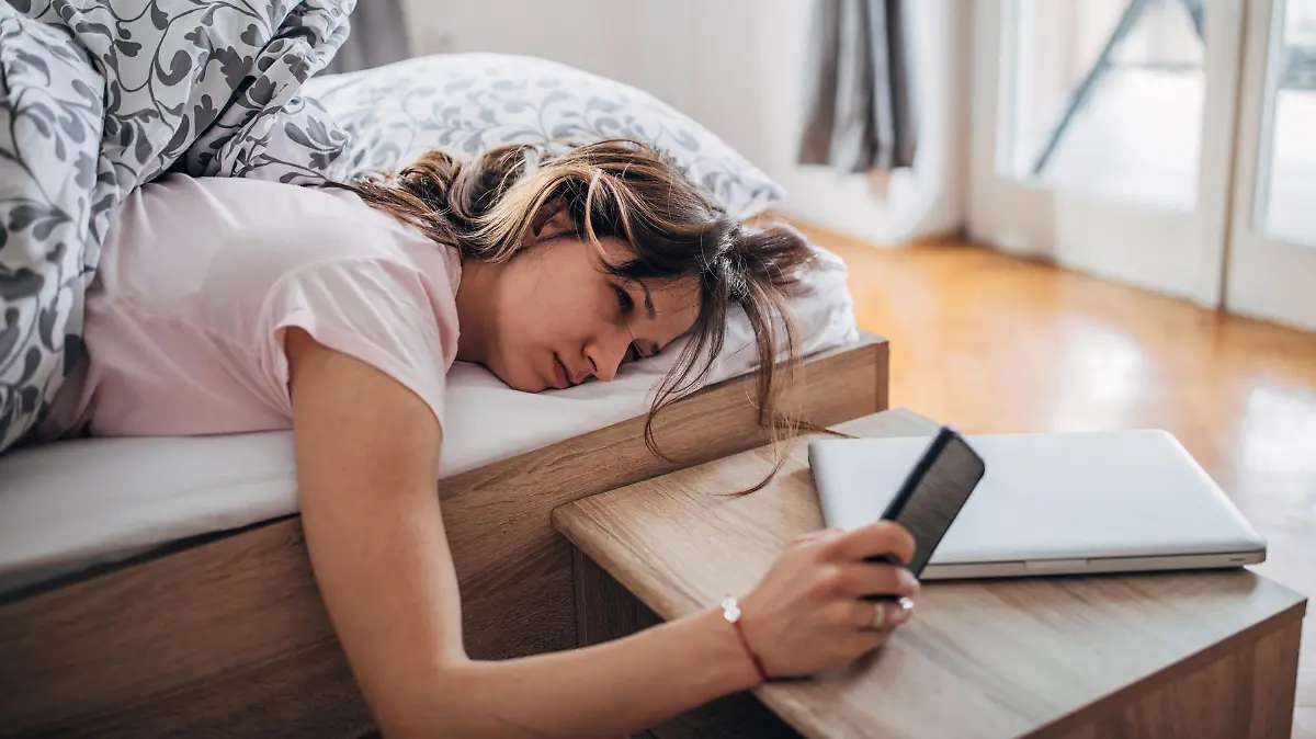 Young woman is waking up and looking at her smart phone.