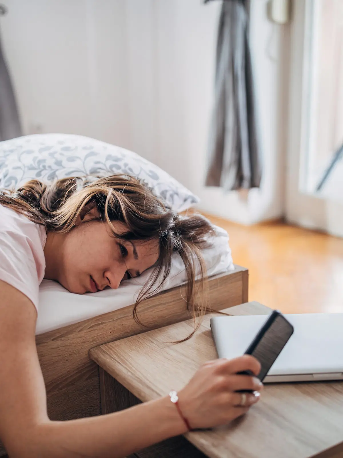Young woman is waking up and looking at her smart phone.