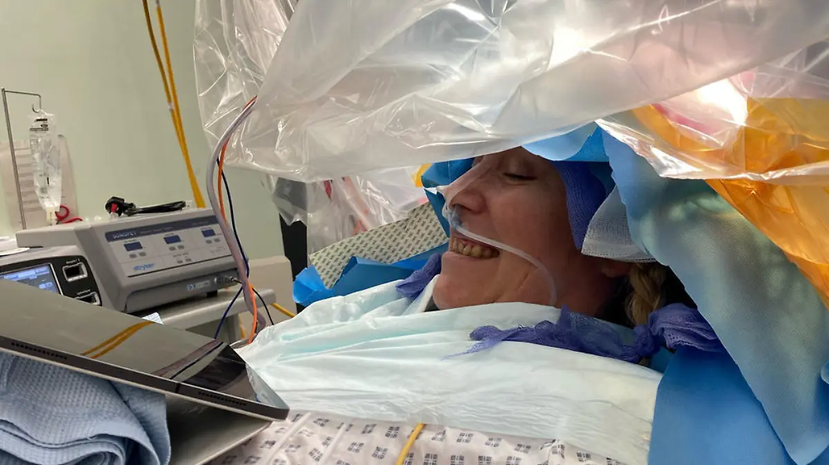 Auf dem OP-Tisch hält Charlotte ein Tablet in der Hand während sie operiert wird.