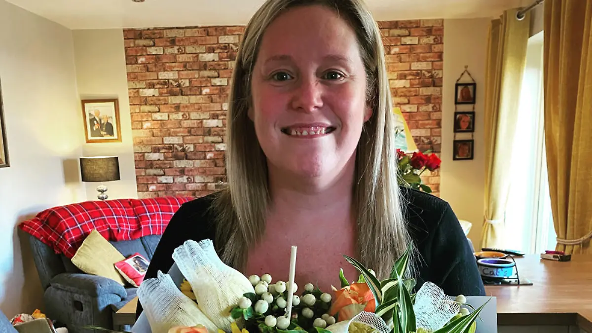Charlotte Hughes hält Blumen in der Hand und lächelt.