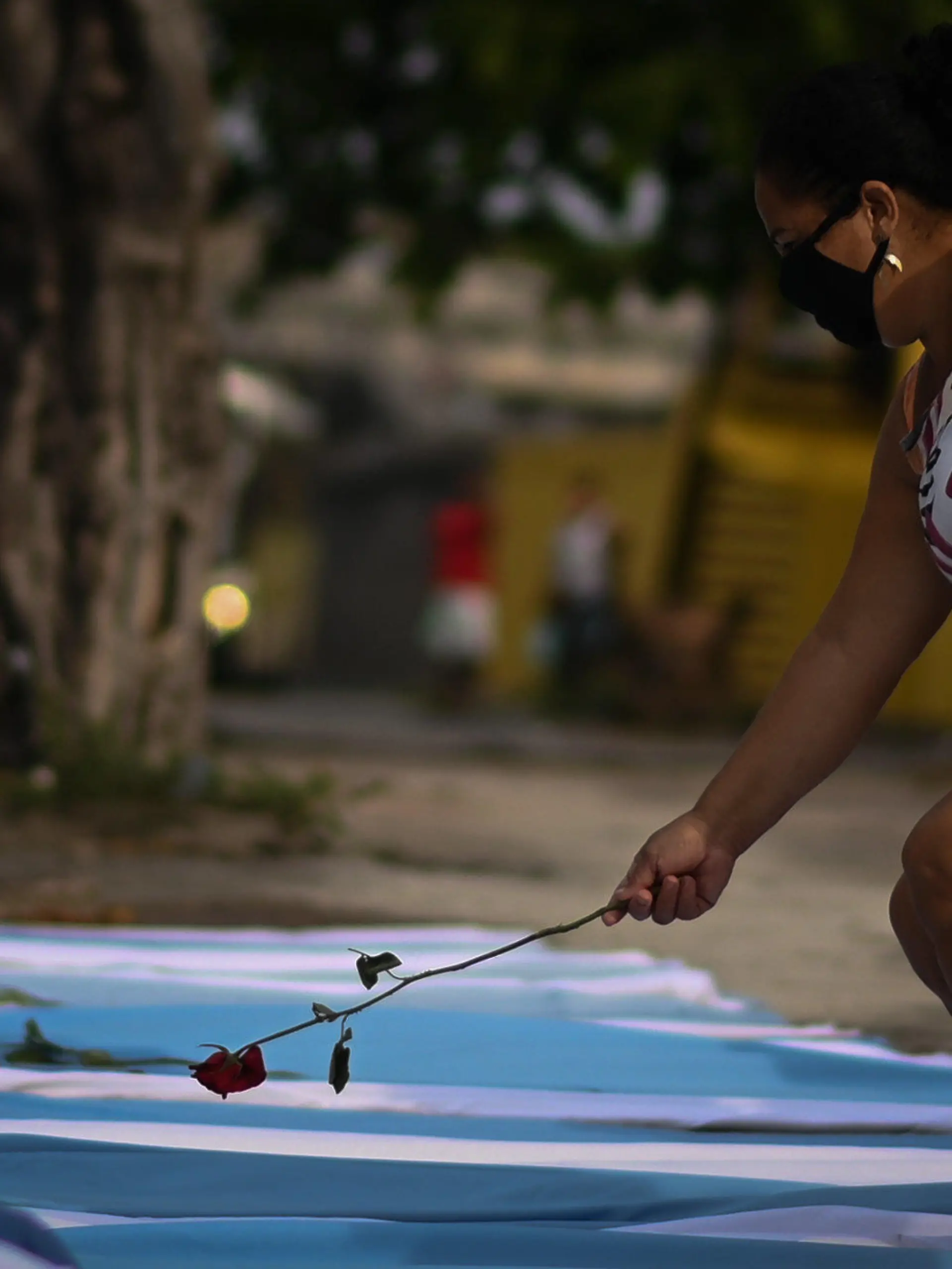 dpatopbilder - 24.03.2021, Brasilien, Acari: Eine Frau legt eine Rose auf eine Bahre mit Laken und Kissen, während eines Protestes im Gedenken an die rund 300.000 Corona-Toten in Brasilien. In Brasilien sind zudem zum ersten Mal mehr als 3000 Menschen an einem Tag nach einer Corona-Infektion gestorben. Foto: Andre Borges/dpa +++ dpa-Bildfunk +++