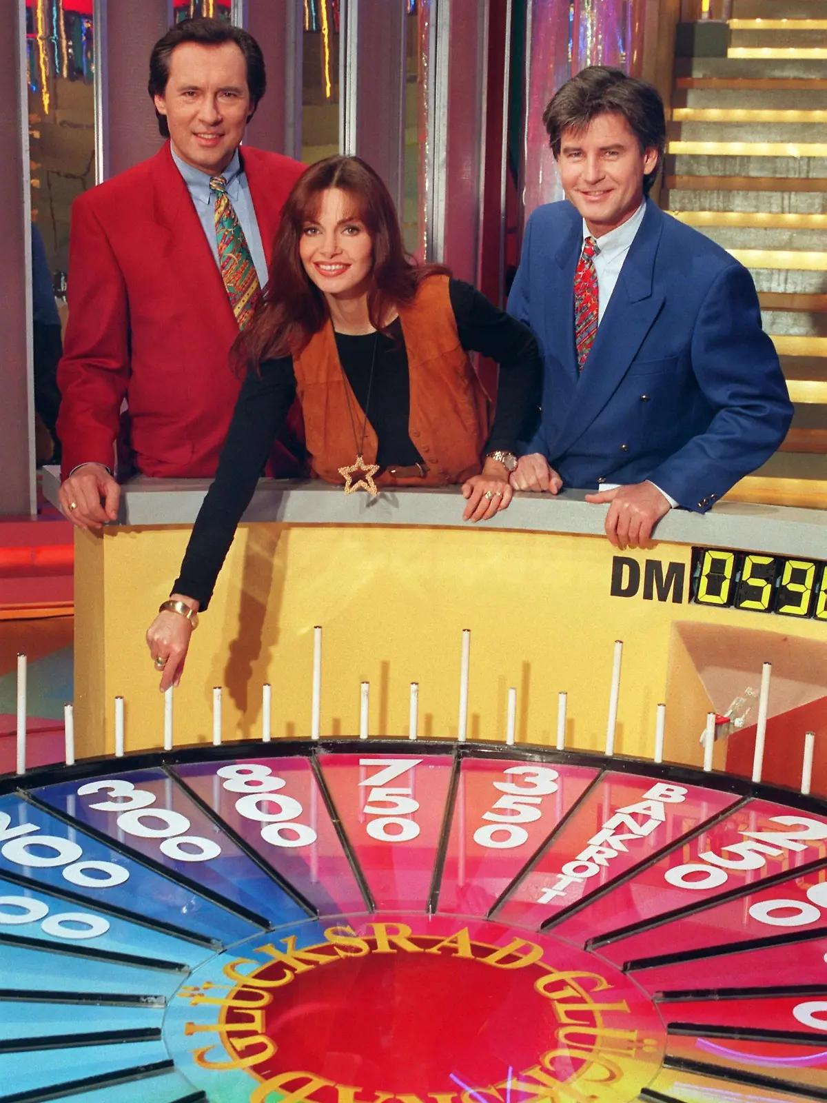 Maren Gilzer, Peter Bond (l) und Frederic Meisner posieren am 10.2.1994 im neuen Studio an der Glücksrad-Scheibe für die Fotografen. Die erfolgreichste deutsche Gameshow ist umgezogen. Seit dem 4. Februar wird die Sendung aus dem neuen und größeren Studio auf dem Gelände des ehemaligen DDR-Fernsehens in Berlin Adlershof ausgestrahlt.