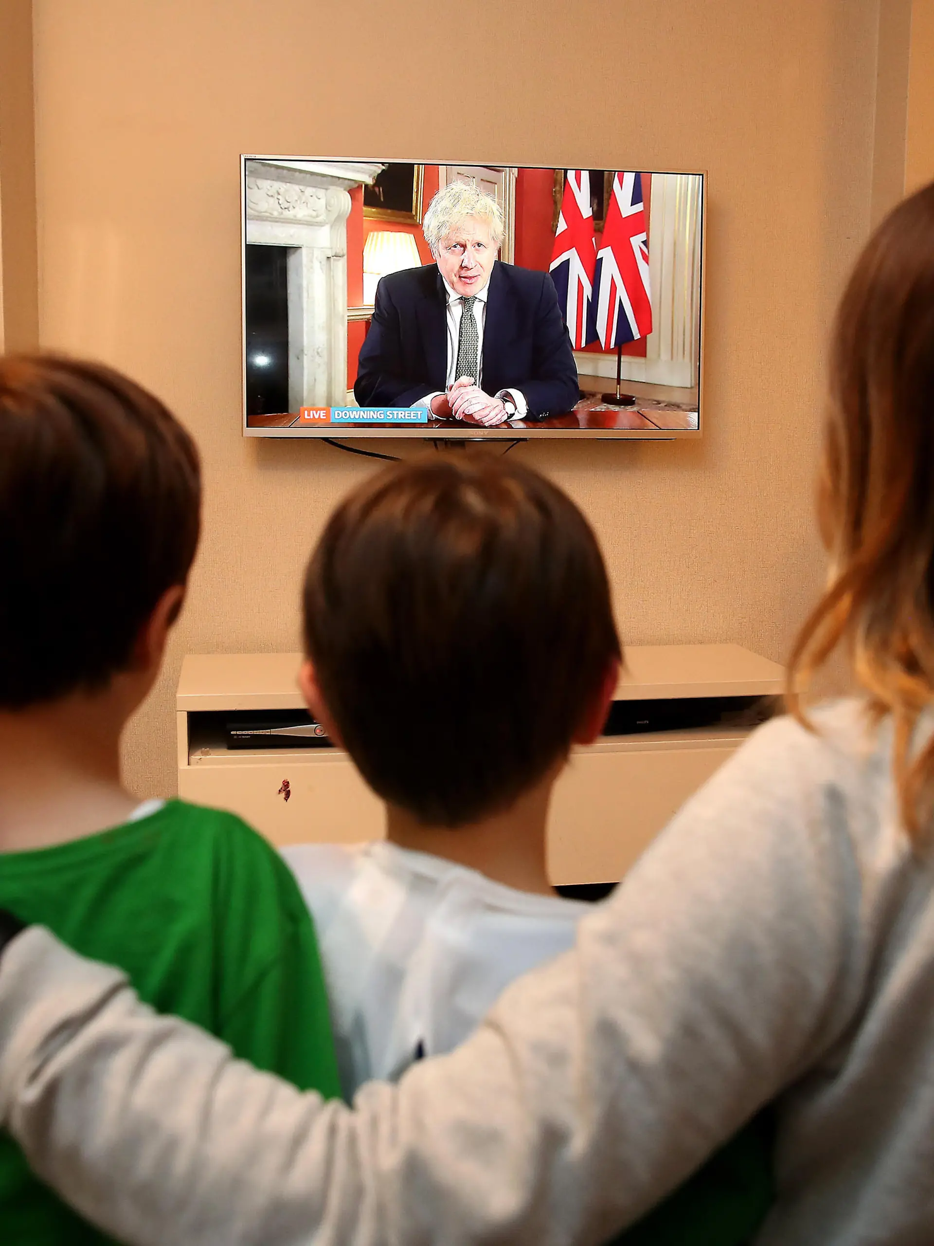 Eine britische Familie sitzt auf dem Sofa und schaut sich eine Nachrichtenübertragung mit Premierminister Boris Johnson im Fernsehen an.