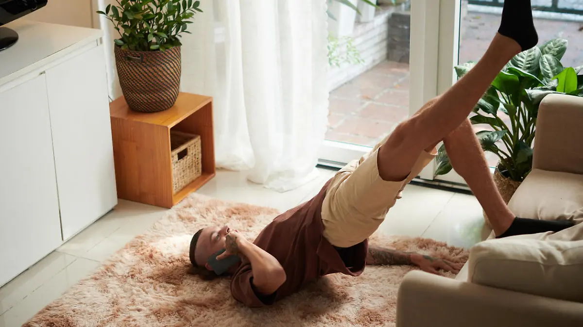 Young man talking on phone, leaning on couch when doing bridge pose at home
