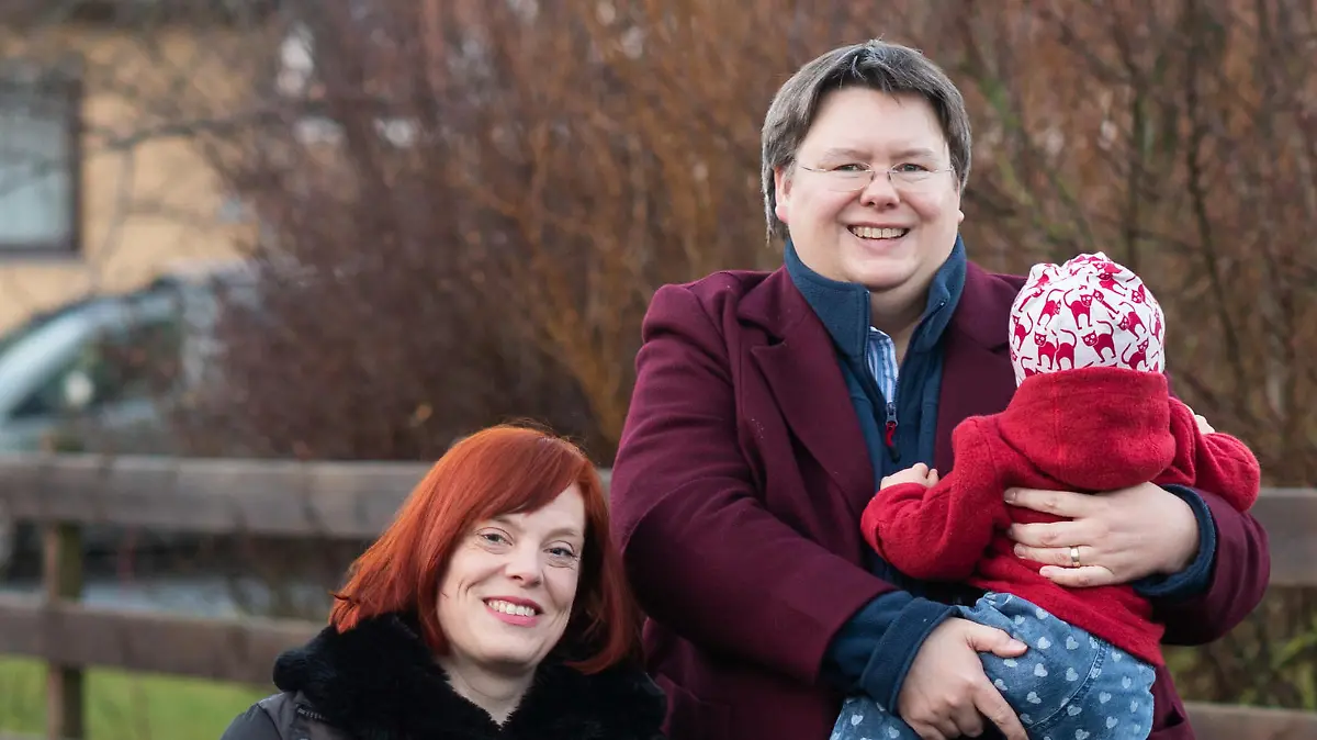 12.01.2021, Niedersachsen, Schellerten: Gesa Teichert-Akkermann (l) und Verena Akkermann, die ihre gemeinsame Tochter Paula (11 Monate alt) auf dem Arm hält, halten ein Plakat mit dem Hashtag #PaulaHatZweiMamas. Familie Akkermann will über Familiengerichte eine Gleichstellung mit heterosexuellen Paaren bei der Elternschaft erreichen. Die leibliche Mutter von Paula und ihre Ehefrau wollen gleichermaßen als rechtliche Mütter der kleinen Paula gelten. Bisher besteht nur die Möglichkeit einer Stiefkindadoption. Foto: Julian Stratenschulte/dpa +++ dpa-Bildfunk +++