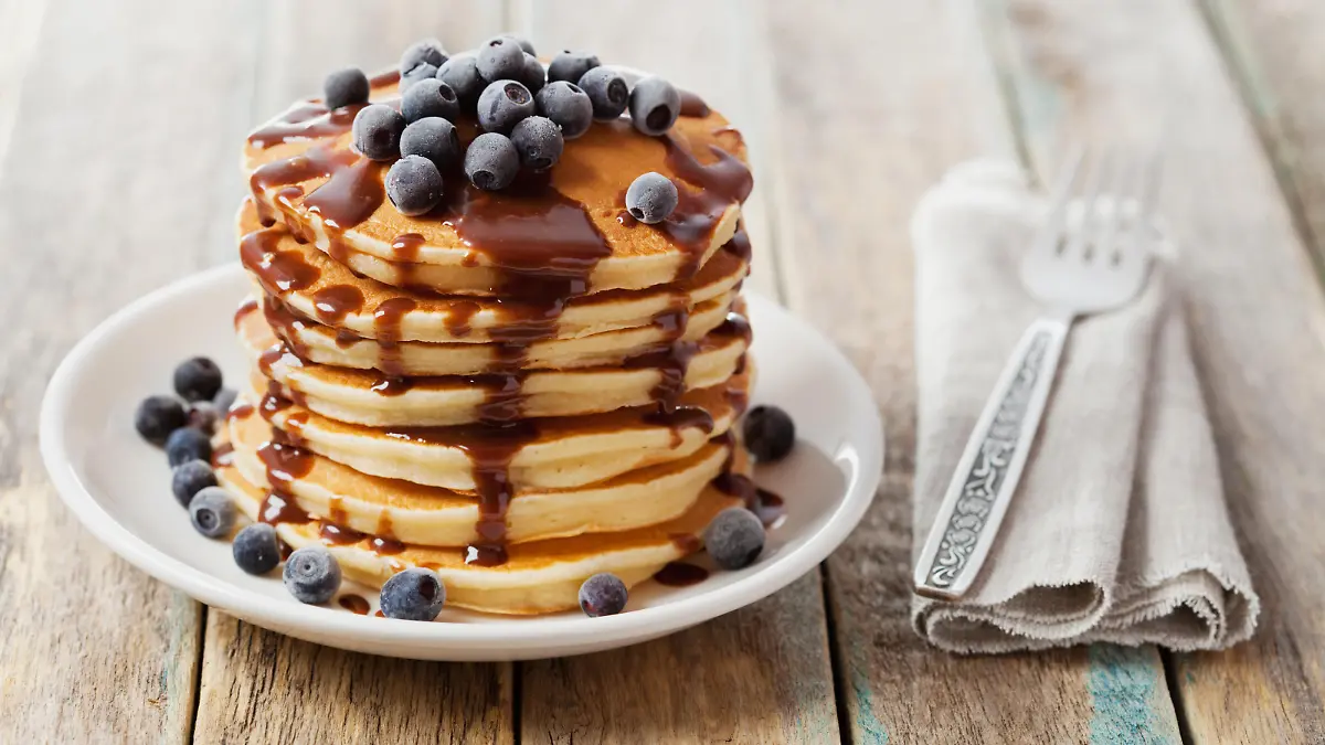 Stack of baked pancakes or fritters with chocolate sauce and frozen blueberries in a white plate on a wooden rustic table, delicious dessert for breakfast