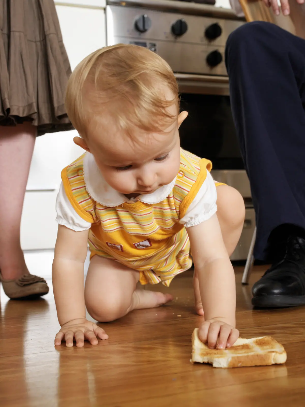 Ein kleines Mädchen krabbelt mit einem Stück Toastbrot in der Hand auf dem Boden herum.
