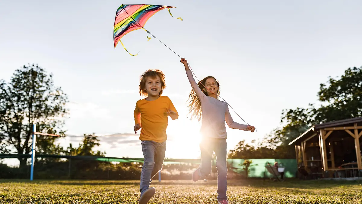 Playful siblings having fun while running with a kite in the backyard. Copy space.