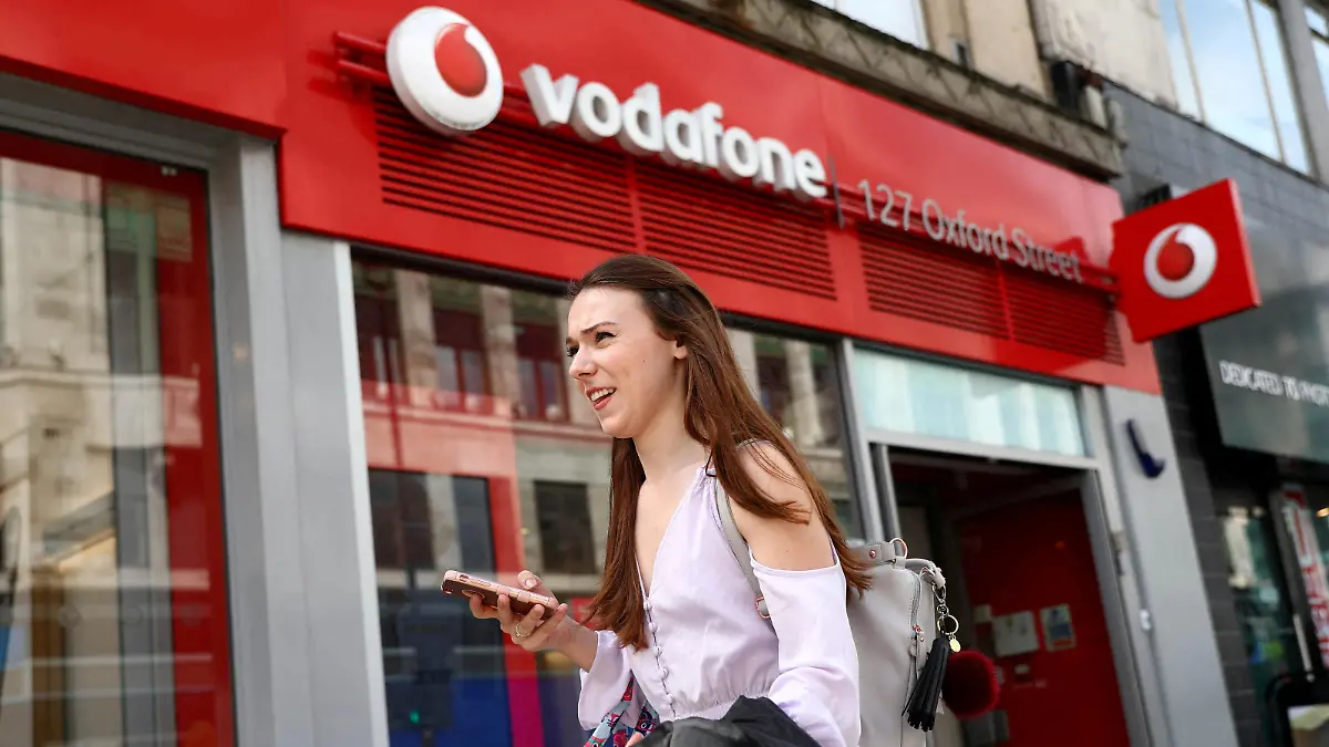 FILE PHOTO: A woman holds a phone as she passes a Vodafone store in London, Britain May 16, 2017. REUTERS/Neil Hall//File Photo