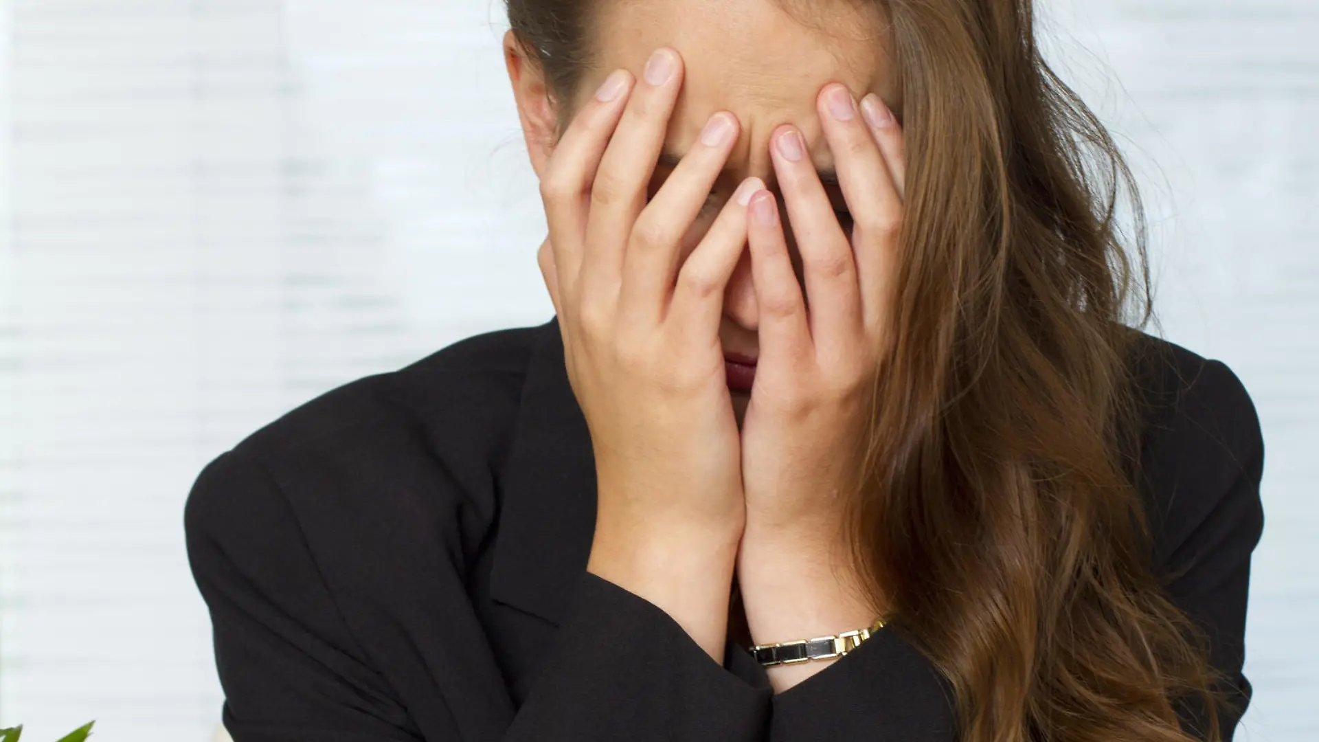Portraet einer jungen Frau am Schreibtisch, mit den Haenden das Gesicht verbergend