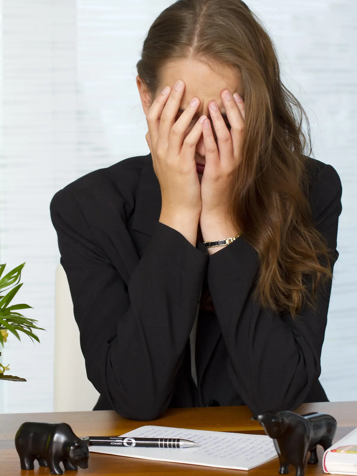 Portraet einer jungen Frau am Schreibtisch, mit den Haenden das Gesicht verbergend