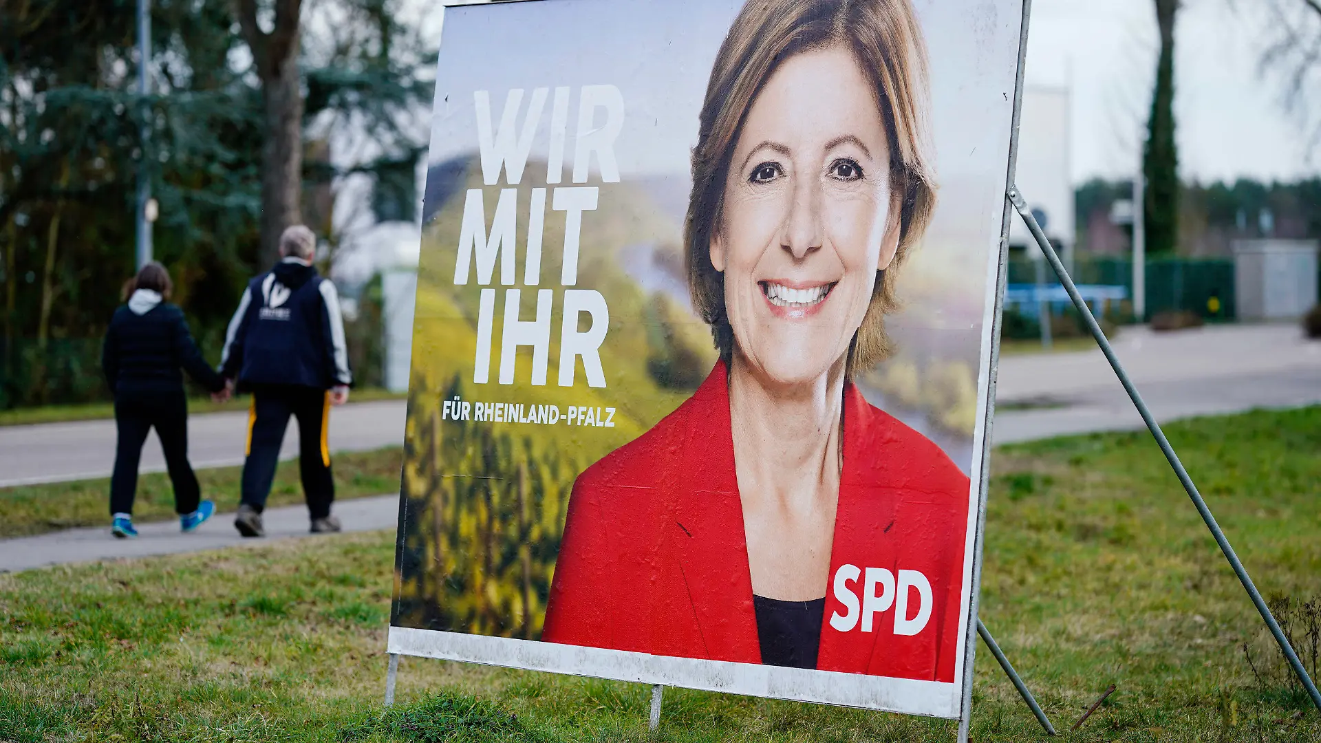 04.02.2021, Rheinland-Pfalz, Haßloch: Zwei Passanten gehen an einem Wahlplakat mit dem Konterfei von Malu Dreyer vorbei, der rheinland-pfälzischen Ministerpräsidentin und Spitzenkandidaten der SPD für die kommende Landtagswahl. (zu dpa: «Wie tickt Haßloch? - Vorwahlstimmung im Mini-Deutschland in der Pfalz») Foto: Uwe Anspach/dpa +++ dpa-Bildfunk +++