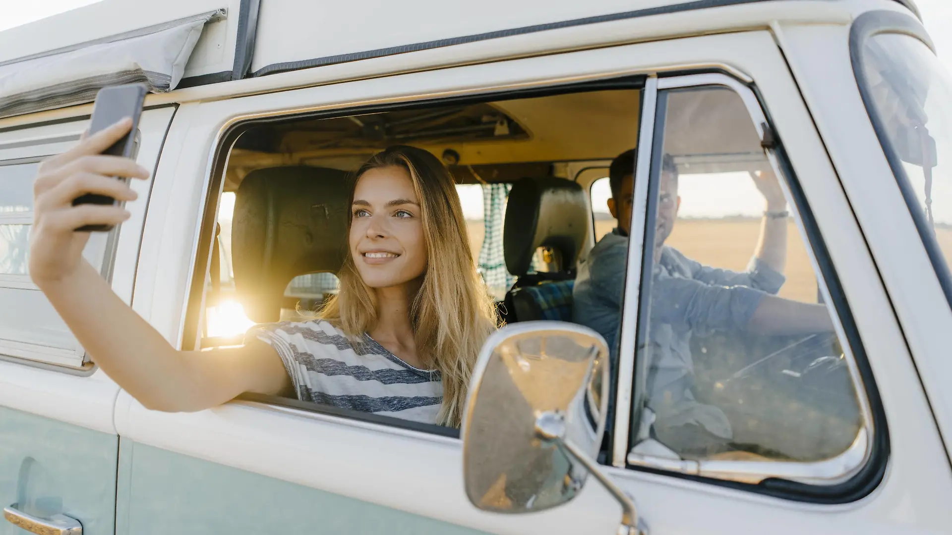 Smiling woman taking a selfie in a camper van with man driving model released Symbolfoto PUBLICATIONxINxGERxSUIxAUTxHUNxONLY GUSF01426