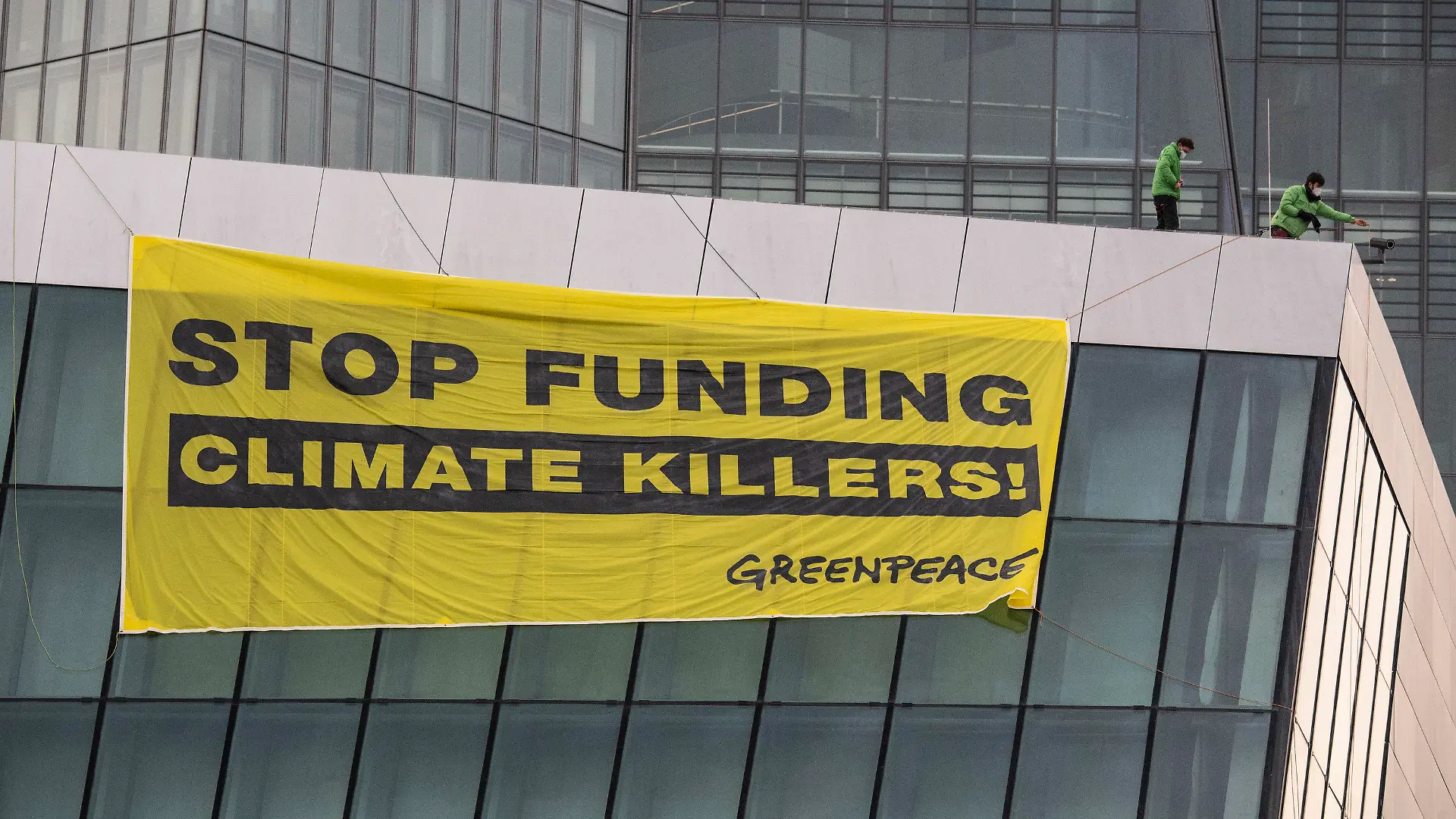 10.03.2021, Hessen, Frankfurt/Main: "Stop funding climate killers" steht auf einem Plakat, das Greenpeace-Aktivisten auf dem Dach der Europäischen Zentralbank (EZB) entrollt haben. Dazu waren zwei Aktivisten mit Gleitschirmen auf dem schwer gesicherten Areal gelandet. Mit der Aktion protestiert Greenpeace am Tag vor der EZB-Ratssitzung gegen die Klimapolitik der EZB. Foto: Boris Roessler/dpa +++ dpa-Bildfunk +++