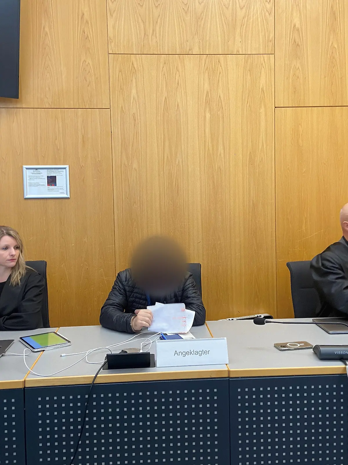 17.04.2025, Baden-Württemberg, Ulm: Ein Angeklagter sitzt zwischen seinen Verteidigern Jana Gieren und Andreas Baier im Gerichtssaal im Landgericht. Der Mann aus dem Alb-Donau-Kreis soll den sexuellen Missbrauch von Kindern auf den Philippinen in Auftrag gegeben und dafür bezahlt haben, sich die schweren Missbrauchshandlungen per Livestream ansehen zu können. Am Donnerstag hat der Prozess begonnen. Foto: Tatjana Bobic/dpa - ACHTUNG: Der Angeklagte wurde auf Wusch seiner Verteidiger gepixelt. Auch Informationen auf einem Zettel, den er hält, wurden aus rechtlichen Gründen gepixelt. +++ dpa-Bildfunk +++